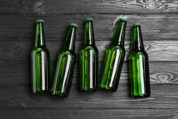 Glass bottles of beer on black wooden background, flat lay