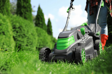 Woman cutting grass with lawn mower in garden on sunny day, closeup