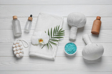 Fototapeta na wymiar Beautiful spa composition with herbal massage bags and different care products on white wooden table, flat lay