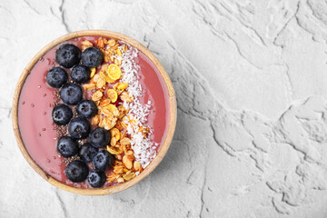 Bowl of delicious fruit smoothie with fresh blueberries, granola and coconut flakes on white textured table, top view. Space for text