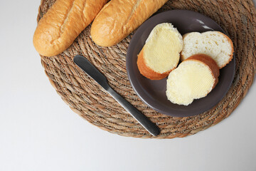 Whole and cut baguettes with fresh butter on white table, top view
