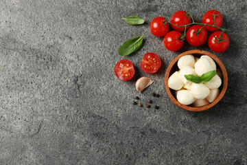 Delicious mozzarella balls in wooden bowl, tomatoes and basil leaves on light gray table, flat lay. Space for text