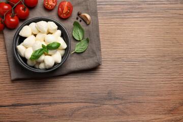 Delicious mozzarella balls, tomatoes and garlic on wooden table, flat lay. Space for text