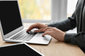 Woman with tablet working on laptop at wooden table, closeup. Electronic document management