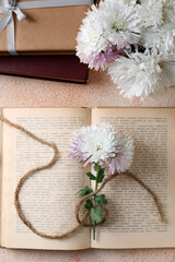 Book with chrysanthemum flowers as bookmark on beige textured background, flat lay