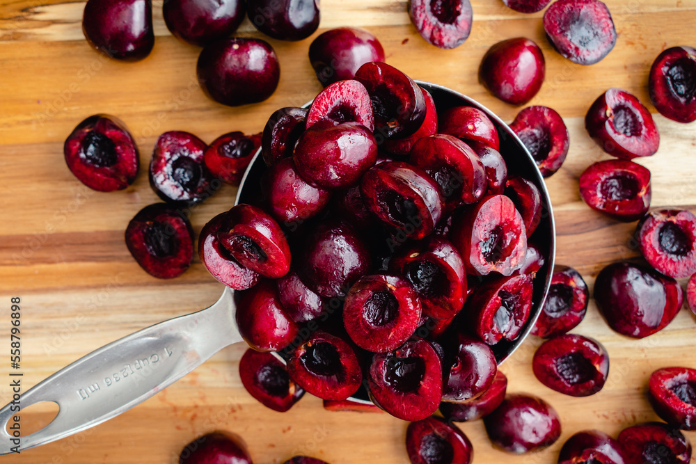 Wall mural halved cherries in an overflowing measuring cup: pittted cherries in a scoop viewed close-up from ab