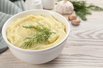 Bowl of tasty mashed potato with garlic and dill on wooden table, closeup. Space for text