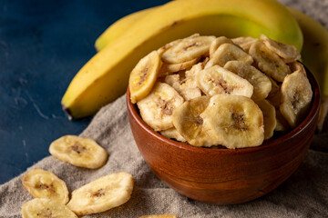 Dried banana chips in a bowl on dark blue background.