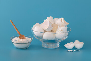 Eggshell, glass containers, wooden spoon, shells, calcium. Blue background. 