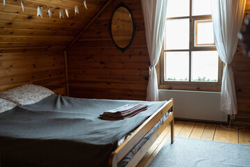 Cozy country hotel room with freshly made double bed in wooden house, nobody. Interior of stylish rustic attic bedroom with low sloping ceiling. Interior design concept
