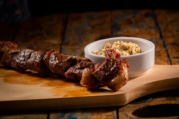 Espetinho de churrasco com farofa em tábua de madeira