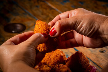 Porção de coxinha em pote vermelho e mão feminina com esmalte vermelho em mesa de madeira