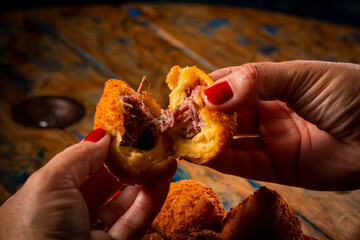 Porção de coxinha em pote vermelho e mão feminina com esmalte vermelho em mesa de madeira