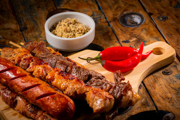 Espetinhos de churrasco em tábua de madeira com acompanhamentos, arroz, vinagrete, farofa e...