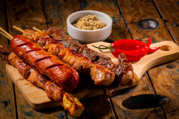 Espetinhos de churrasco em tábua de madeira com acompanhamentos, arroz, vinagrete, farofa e maionese