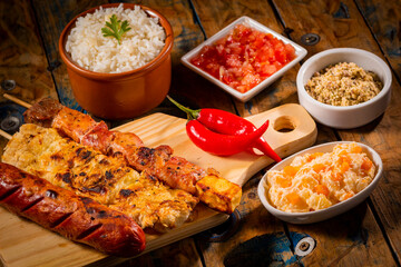 Espetinhos de churrasco em tábua de madeira com acompanhamentos, arroz, vinagrete, farofa e...