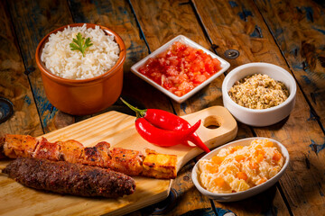 Espetinhos de churrasco em tábua de madeira com acompanhamentos, arroz, vinagrete, farofa e maionese