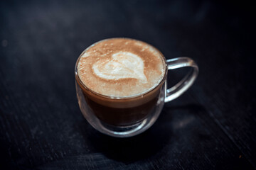 Latte art of a heart in a glass mug resting on a black wooden table