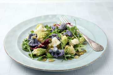 Delicious salad with cauliflower and pumpkin seeds served on white tiled table, closeup
