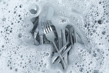 Washing silver spoons, forks and knives in water with foam, flat lay