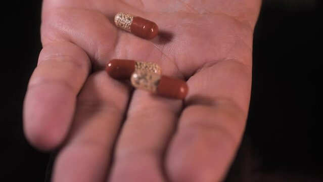 The man opens his hand and there are a lot of pills: enzyme, pancreatic treatment. Close-up shot on a black surface.