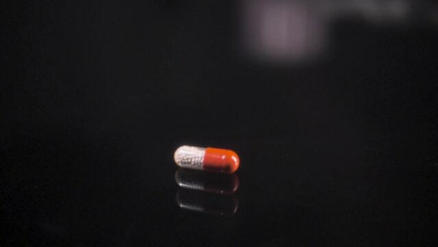 Pill falling down on a black glass surface, mirror surface with a reflection on black background. Spinning and rotating. Solwmotion.