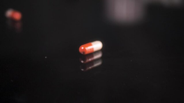 Pills falling down on a black glass surface,  mirror surface with a reflection on black background. Spinning and rotating. Scene C.