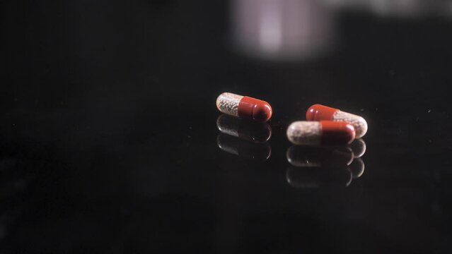 Pills moving on a black glass surface,  mirror surface with a reflection on black background. Spinning and rotating. Solwmotion.