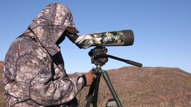 Hunter using a telescope to look for animals in full camo