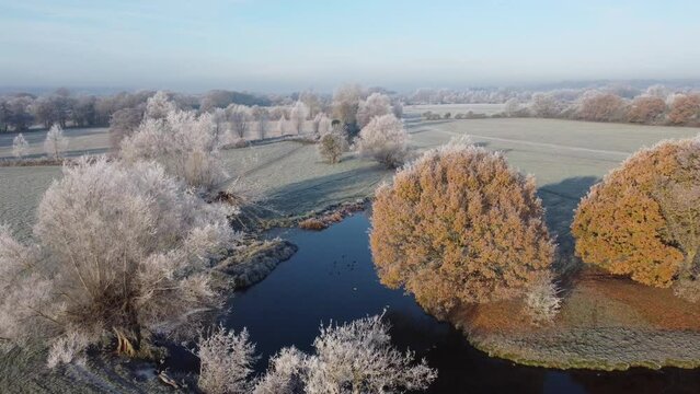 Aerial footage moving forwards over the river stour and trees covered in hoar frost early one winter morning.
