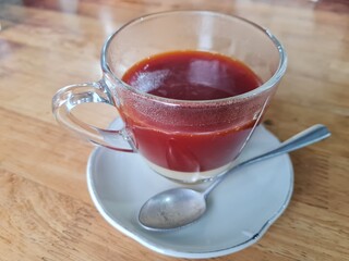 Dark brown hot tea in a glass saucer is placed on the table.