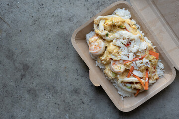 Rice and scrambled eggs topped with seafood in box, top view