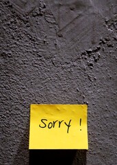 Grey rough textured wall with yellow notepad/post-it written SORRY,concept of making apology to someone
