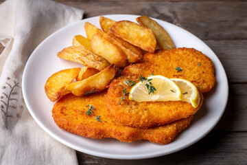 Chicken schnitzel with sauce, fried potatoes and lemon in a plate