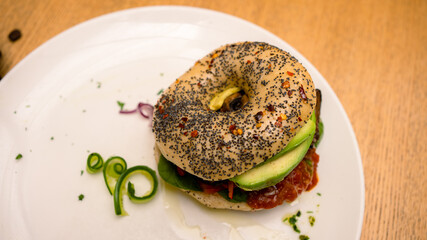 Vegan and vegetarian-friendly toasted chia seed sourdough bagel topped with avocado, shredded carrots, eggplant, red onions, sun-dried tomatoes, and spinach leaves with cappuccino on the side.