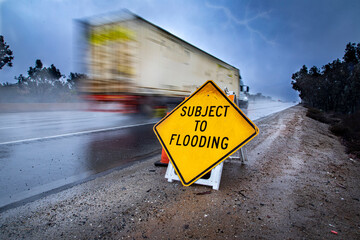 Road Sign stating Subject to Flooding with rainy highway in the bacground
