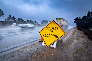 Road Sign stating Subject to Flooding with rainy highway in the bacground