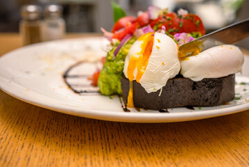 Breakfast or brunch plate of rye sourdough bread,smashed avocado with lemon oil, tomatoes and two poached eggs drip, decorated with editable flowers and a cappuccino cup on the side