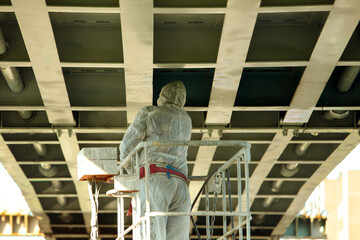 a worker in protective overalls paints the metal surface of the bridge while standing on a hydraulic lift