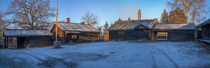 Fototapeta premium Old log house farm houses in a park, a low winter solstice a sunny and snowy day in Stockholm