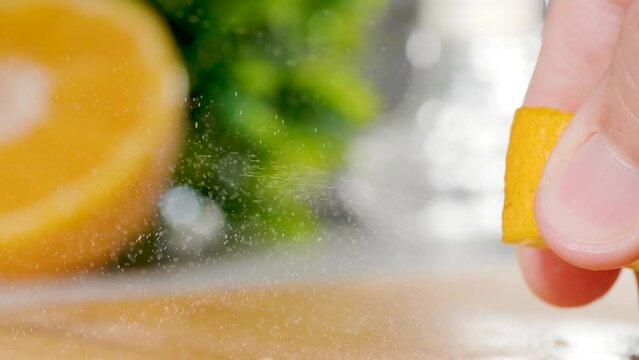 Fingers squeezing orange zest releasing Citrus particles in Slow motion, Extreme Close-up