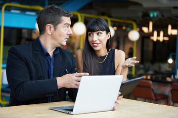 businesswoman and businessman or couple talking and working together with laptop computer in a cafe