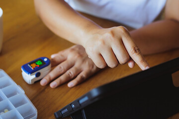 Asian woman self testing for blood oxygen levels with pulse oximeter monitor on her finger at home and record result in the tablet.