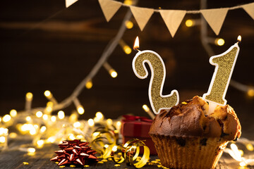 Number 21 gold burning candle in a cupcake against celebration wooden background with lights....