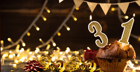 Number 31 gold burning candle in a cupcake against celebration wooden background with lights....