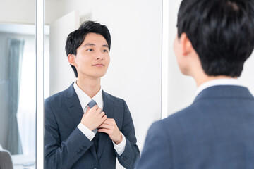 洗面所で鏡を見てネクタイを締める若いビジネスマン（朝・出勤準備）