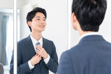 洗面所で鏡を見てネクタイを締める若いビジネスマン（朝・出勤準備）