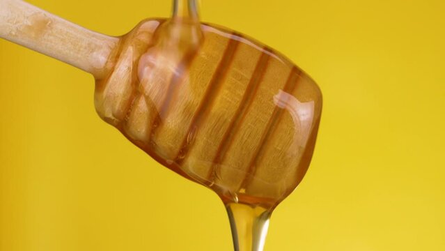 Close-up of Honey dripping from wooden honey dipper on yellow background. macro shot