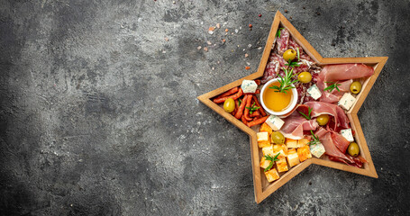 Antipasto platter with ham, prosciutto, salami, cheese, crackers and olives on the board in the form of a Christmas star. Christmas table