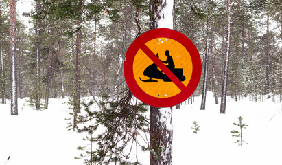 No snowmobile access road sign against tree trunk in snowy winter landscape of Finland.